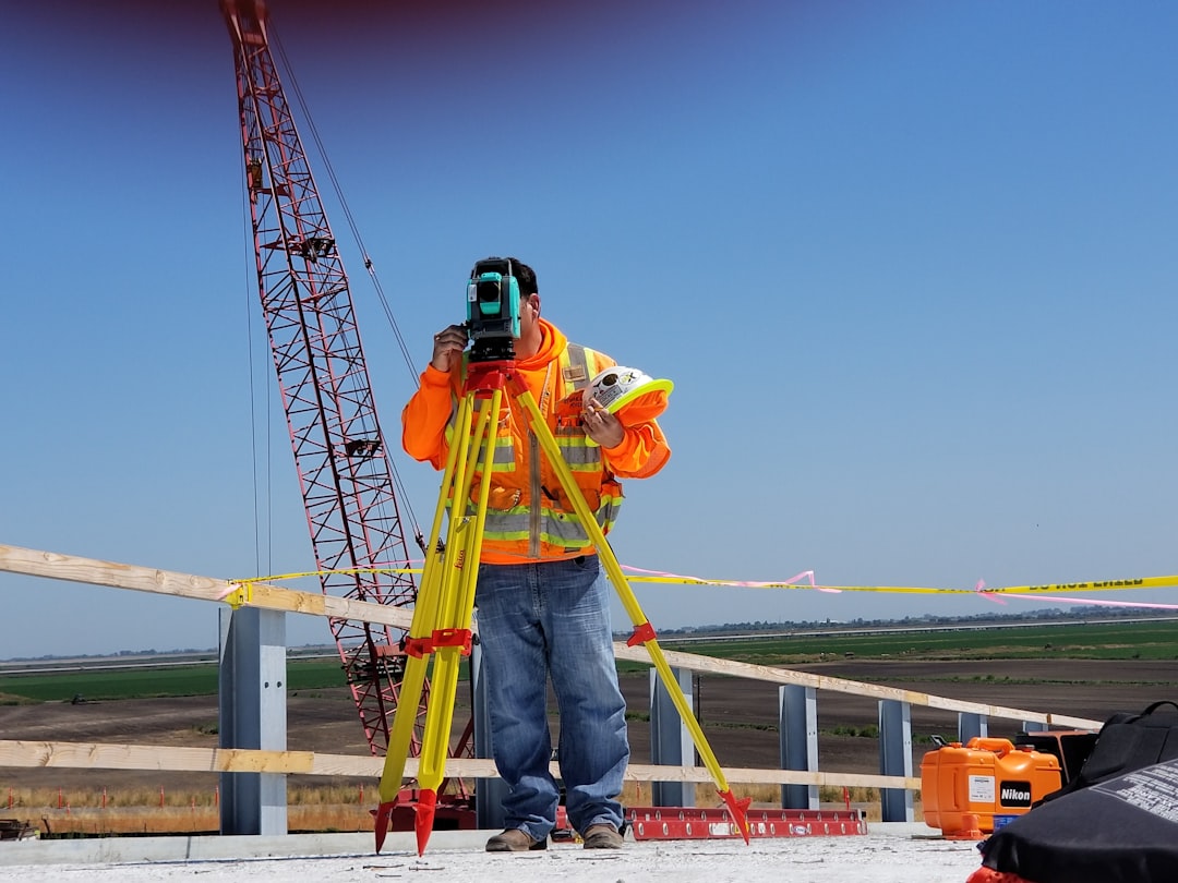 worker using a laser level on a dirt pad to verify elevation - site prep for pole barn
